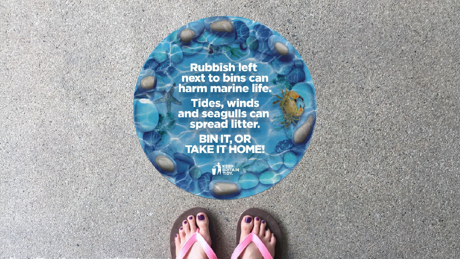 A marine scene with the words 'Bin it or take it home' in a circular floor sign.